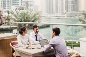 Business meeting on modern balcony in Dubai Marine . Three people representing their companies and talking about cooperation.